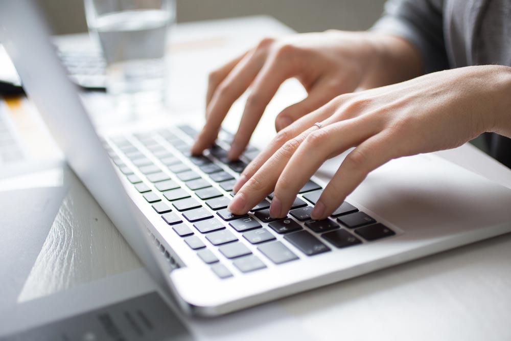 Close-up of female hands working on laptop at desk